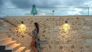 A woman walking down a staircase with stone walls and two wall-mounted lights. - Kritiki Spilia - Home & Spa (Prines)
