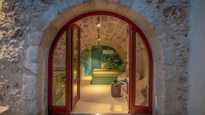 An arched doorway leading into a room with a bed, a small stool, and a green wall. - Kritiki Spilia - Home & Spa (Prines)