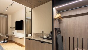 A modern hotel room with a wooden floor, a flat-screen TV mounted on the wall, a small kitchen area with a coffee machine, and a seating area with a chair and a sofa. - Park Inn By Radisson Jalandhar (Jalandhar)