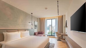 A modern hotel room with a large bed, a flat-screen TV, a seating area, and a view of the city through large windows. - Park Inn By Radisson Jalandhar (Jalandhar)