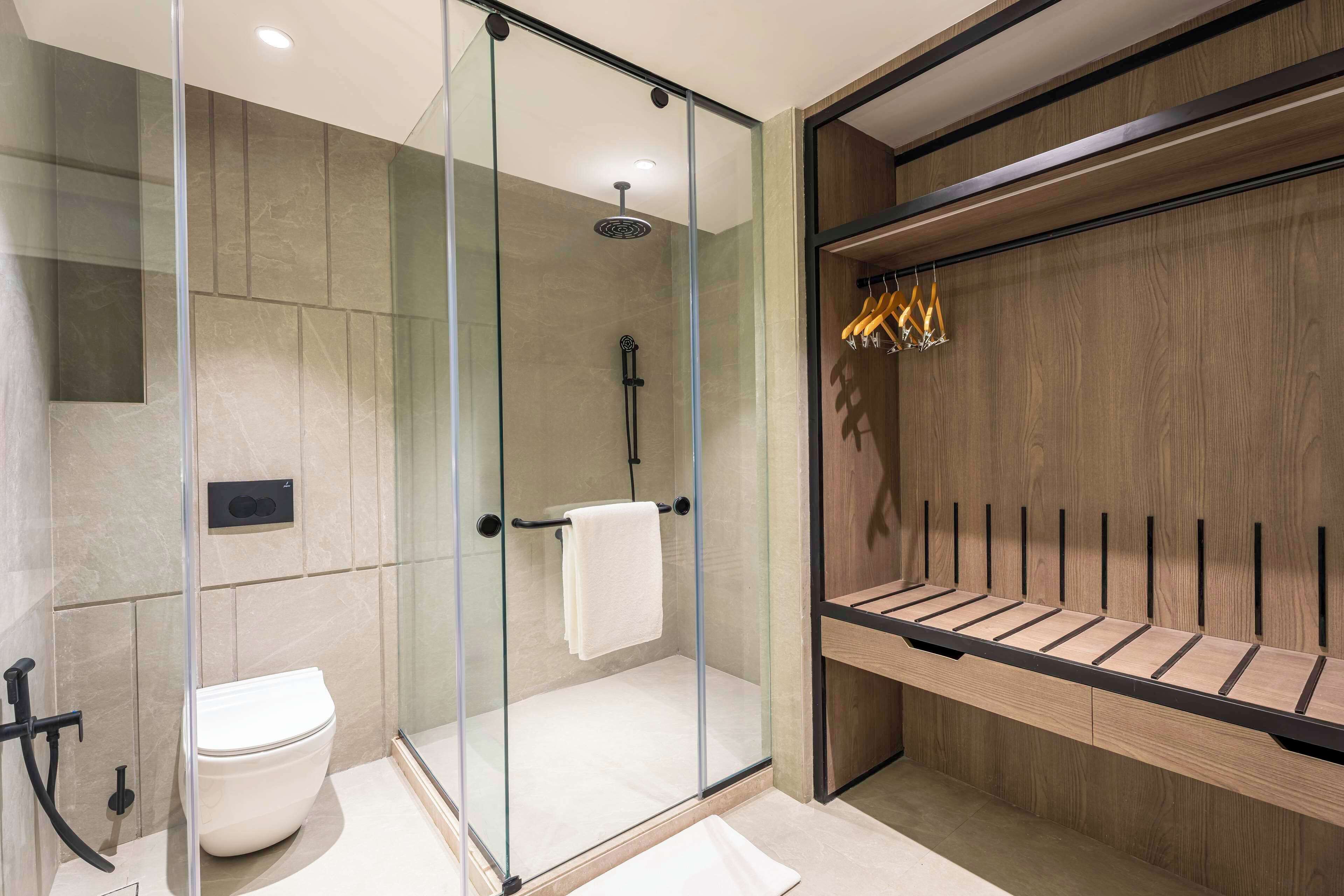 Une salle de bain moderne avec une douche à parois de verre, des toilettes et un meuble-lavabo en bois doté d’un porte-serviettes.