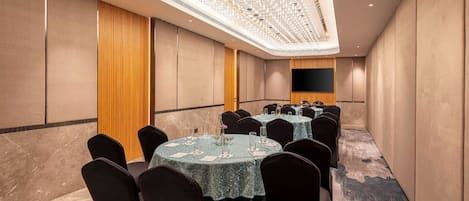 Un salón de conferencias con mesas redondas, sillas negras y una pantalla grande en la pared.