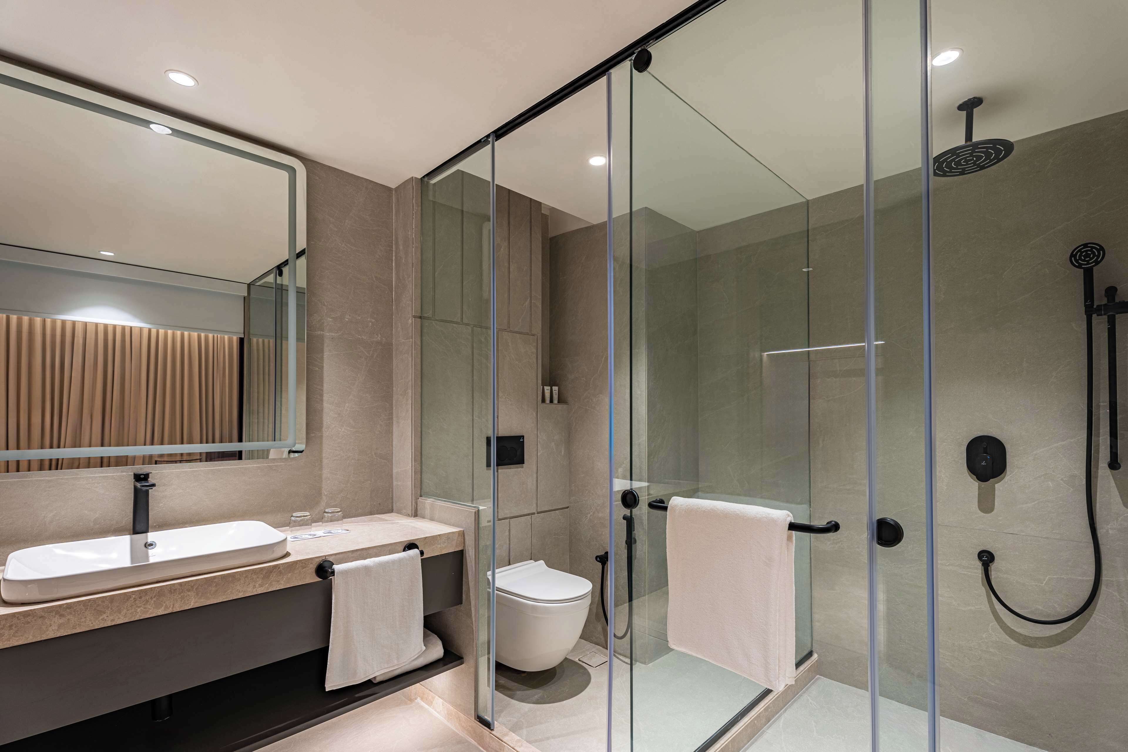 Un baño moderno con ducha de vidrio, un lavabo con espejo y un inodoro.