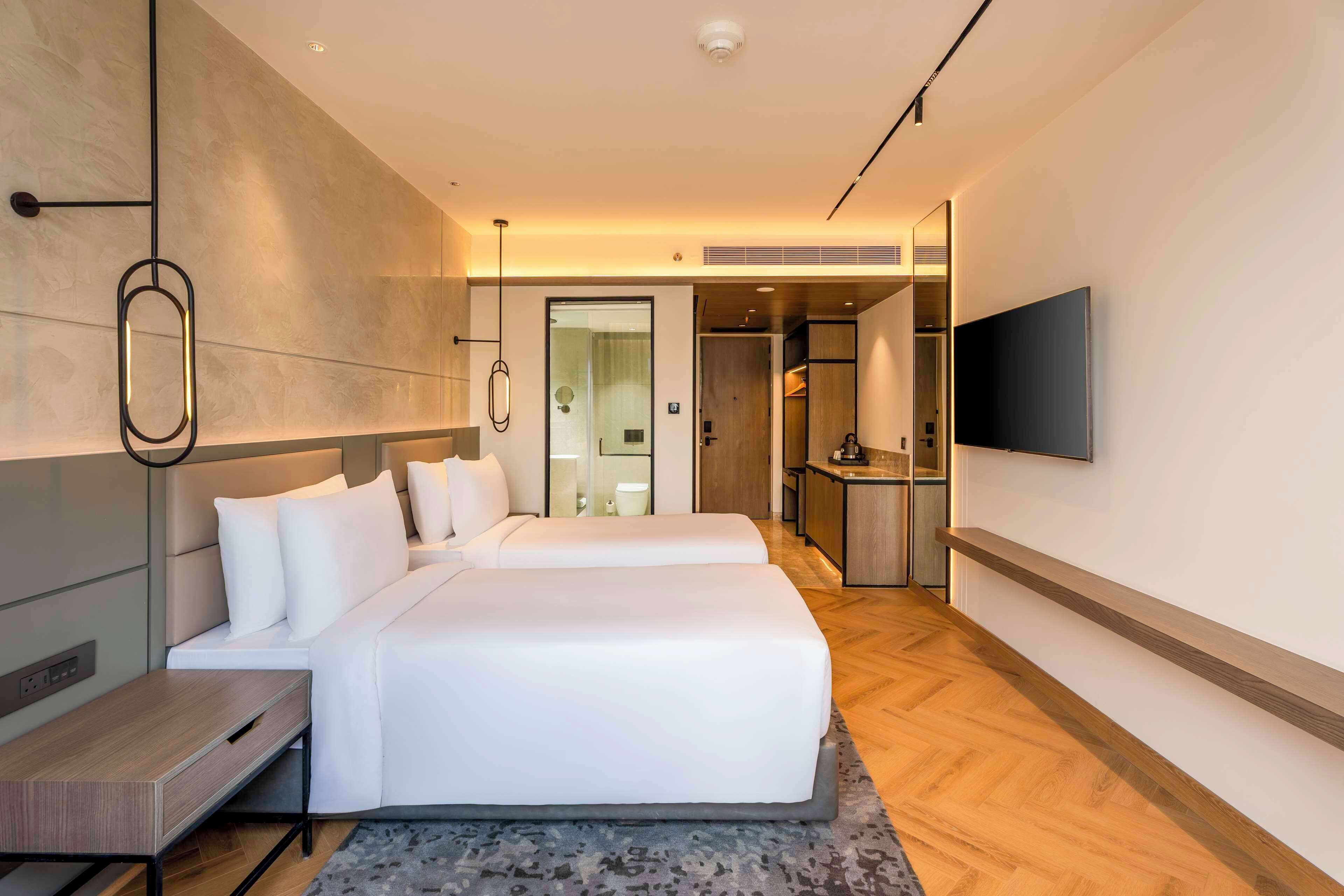 Una habitación de hotel moderna con una cama grande, un escritorio, un televisor de pantalla plana y un baño visible a través de una puerta abierta.