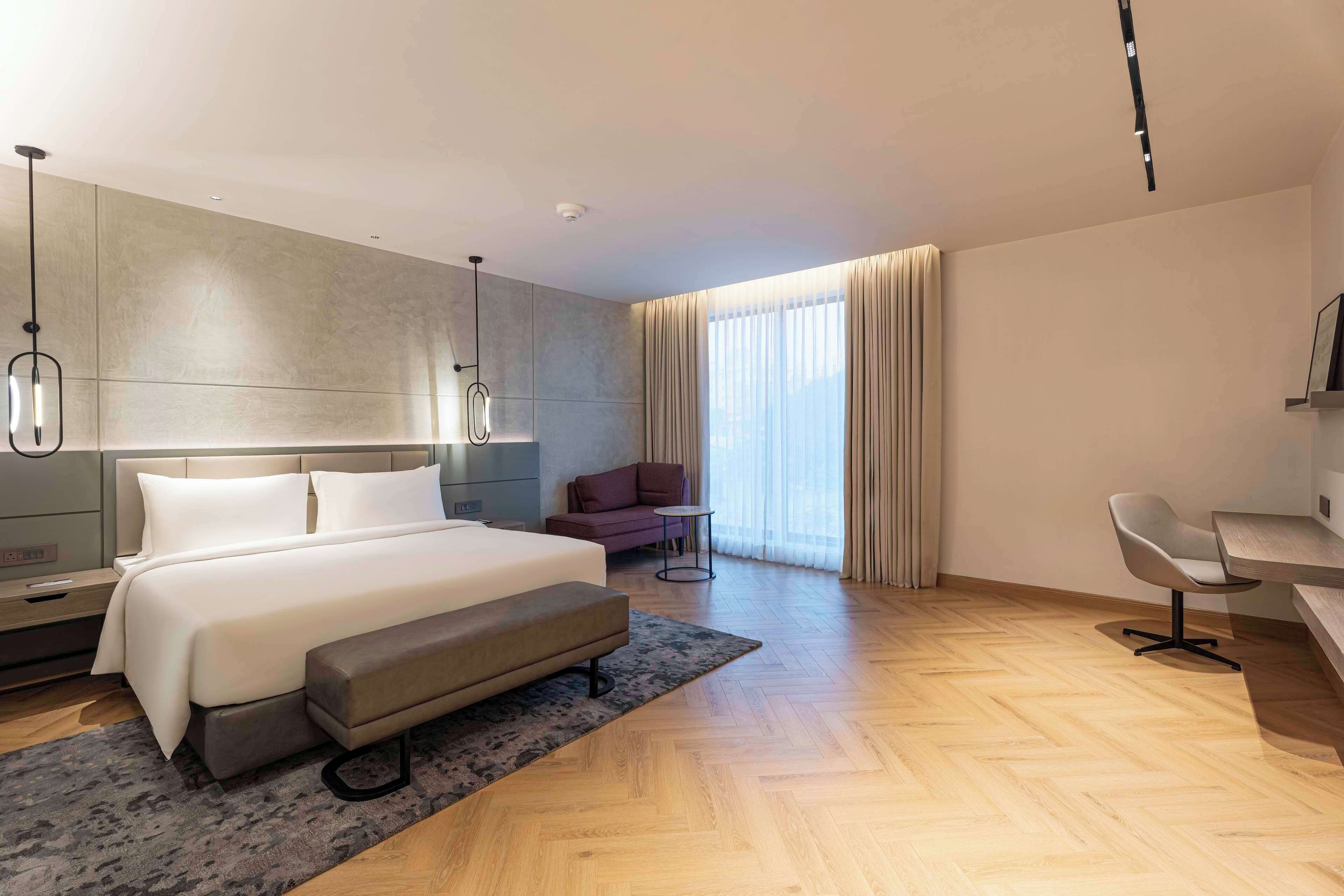 A modern hotel room with a large bed, a desk, a chair, and a sofa.
