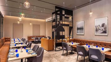 A modern dining area with long tables, cushioned seating, and pendant lighting.