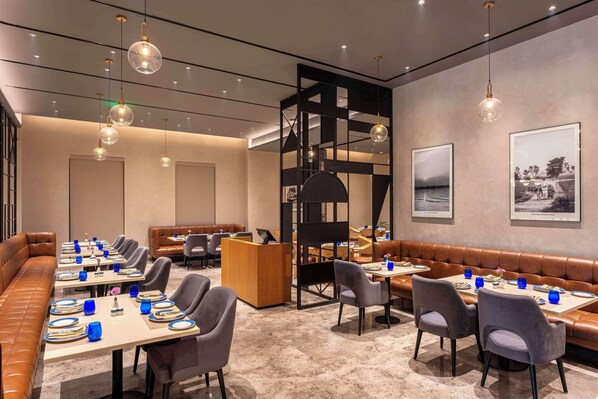 A modern dining area with long tables, cushioned seating, and pendant lighting.