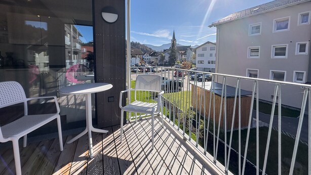 En balkon med bord og stole, udsigt over en gade og bygninger.