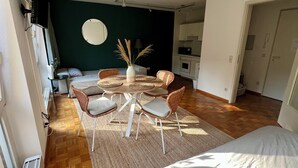 A compact living space with a bed, a dining table with chairs, a kitchen area, and a dark green accent wall. - TheFairSpot - Quiet apartment right next to Nordpark / 5 min to the trade fair and arena (Düsseldorf)