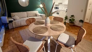 A modern living room with a round dining table, wicker chairs, a sofa, and a kitchen in the background. - TheFairSpot - Quiet apartment right next to Nordpark / 5 min to the trade fair and arena (Düsseldorf)