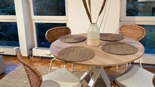 A dining area with a round table, wicker chairs, and a vase with pampas grass. - TheFairSpot - Quiet apartment right next to Nordpark / 5 min to the trade fair and arena (Düsseldorf)
