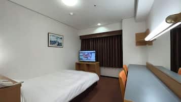 Habitación de hotel con una cama individual, un escritorio con silla, un televisor sobre un soporte de madera, una ventana con cortinas e iluminación montada en la pared.