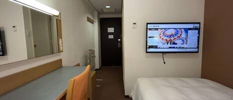 A hotel room with a bed, a desk, a chair, a mirror, a television, and a door.