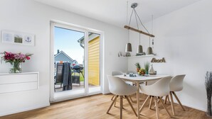 Une cuisine moderne avec un coin repas, un plancher en bois et une grande porte-fenêtre coulissante donnant sur une terrasse extérieure.