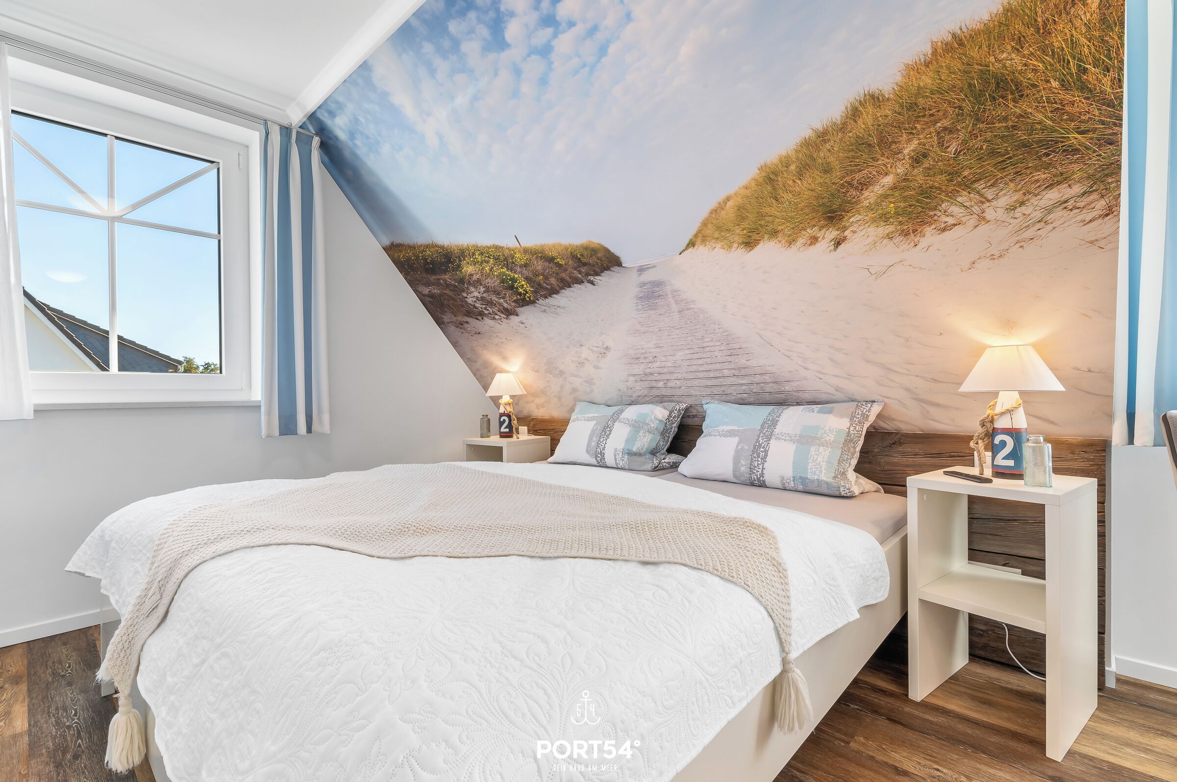 Camera da letto con un letto grande, due comodini con lampade, una finestra e un affresco raffigurante una spiaggia.
