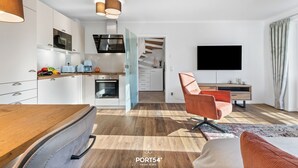 A modern kitchen with white cabinets, a wooden countertop, and a built-in oven. There is a dining area with a wooden table and a chair, and a TV mounted on the wall. - Pier 12b - for 4 persons, parking space, quiet location, modern, cosy terrace (Büsum)