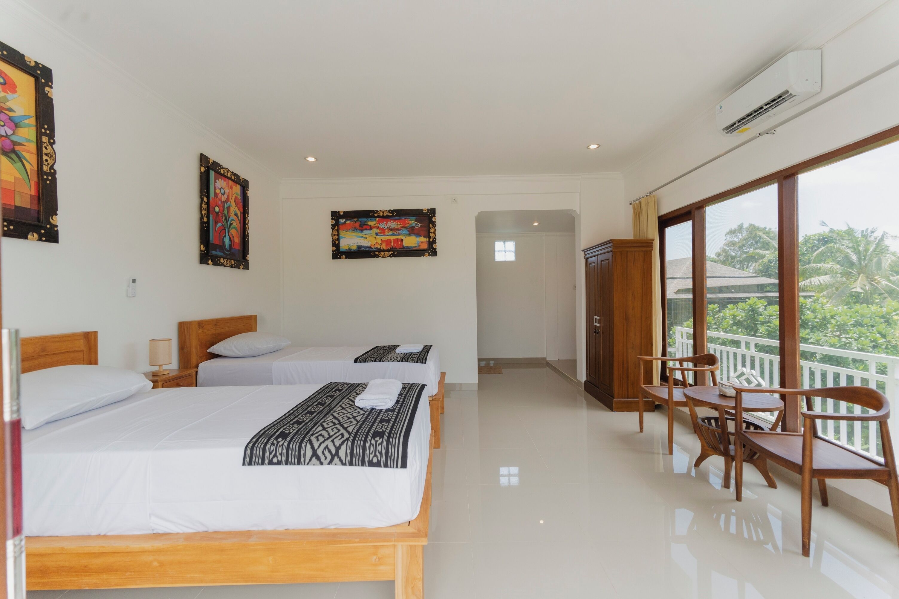 A hotel room with two beds, a balcony with wooden furniture, and artwork on the walls.