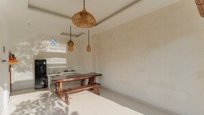 A room with a wooden table and bench, a hanging woven light fixture, and a white wall. - Hotel Anyar Teges (Ubud)