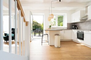 Ett modernt kök med vita skåp, ett trägolv och ett fönster med utsikt över grönområden.