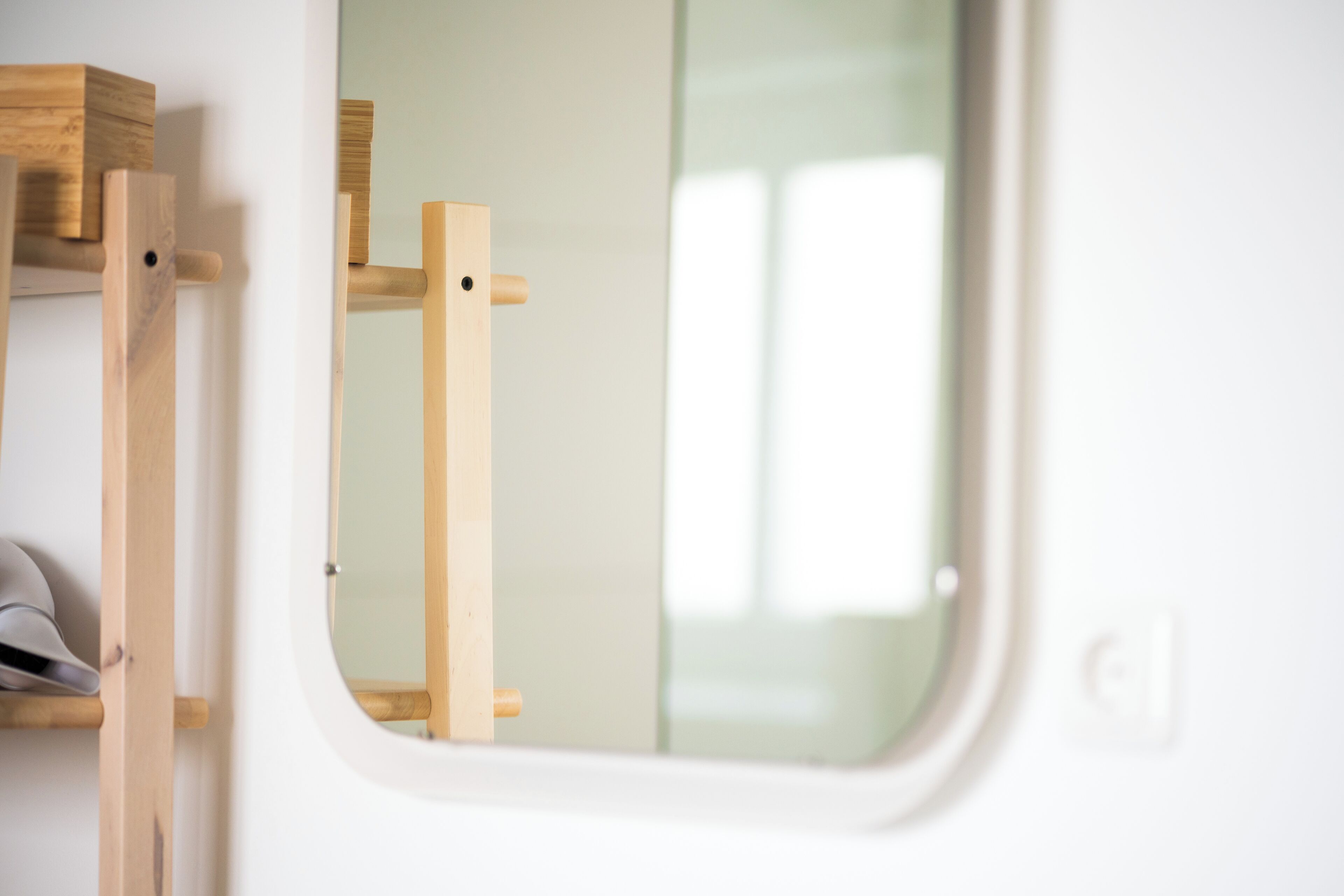 A white bathroom with a wooden shelf and a mirror.