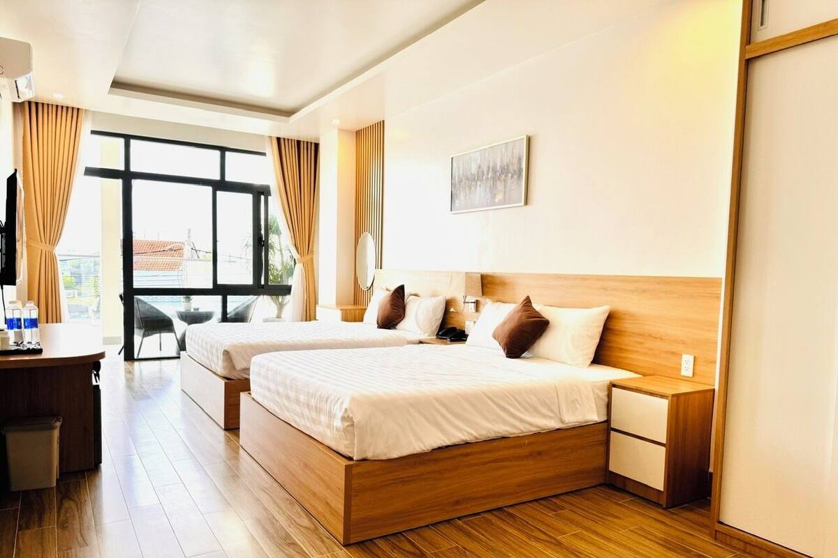 A hotel room with two beds, a desk, and a view of the outdoors.