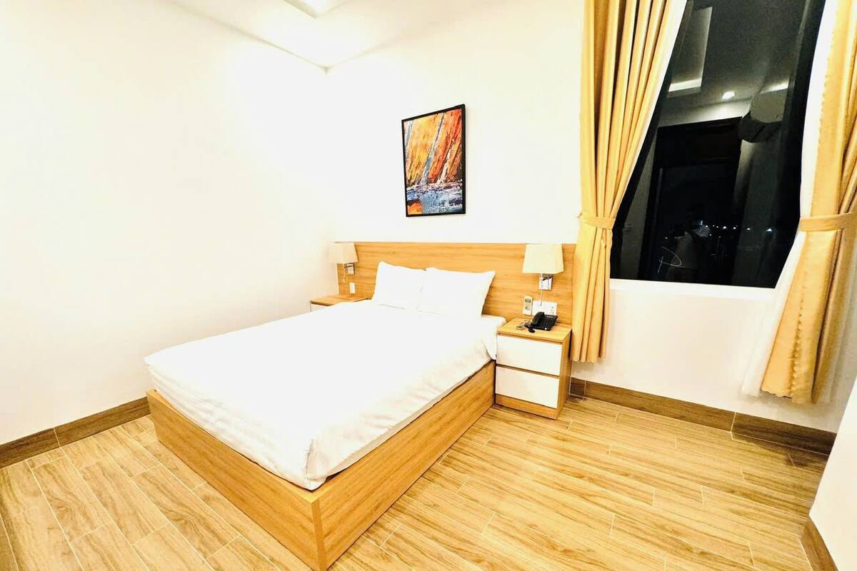 A hotel room with a wooden bed, a nightstand with a lamp, and a window with curtains.
