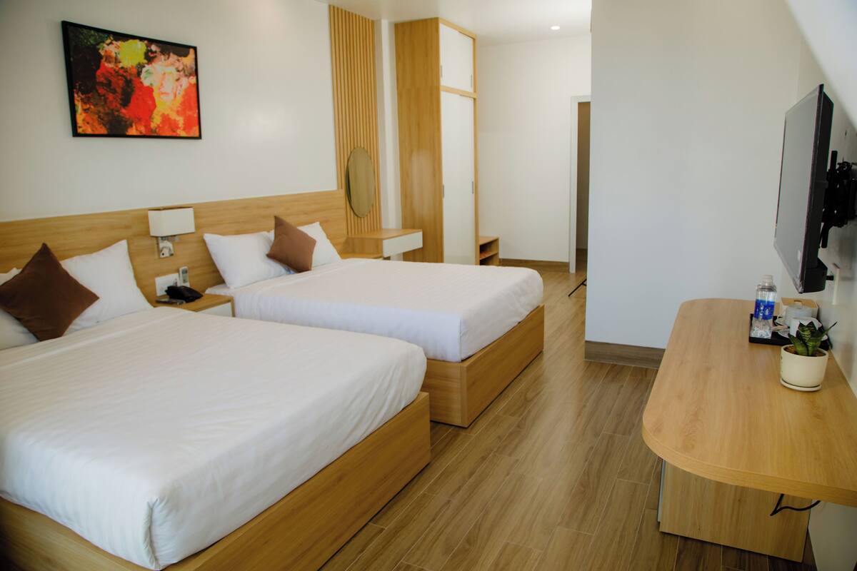 A hotel room with two beds, a wooden desk, a TV, and a painting on the wall.