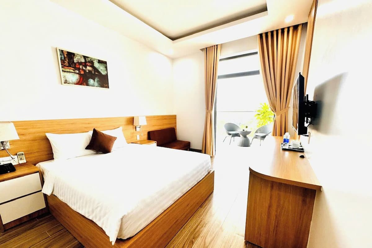 A hotel room with a large bed, a wooden desk, a flat-screen TV, and a painting on the wall.