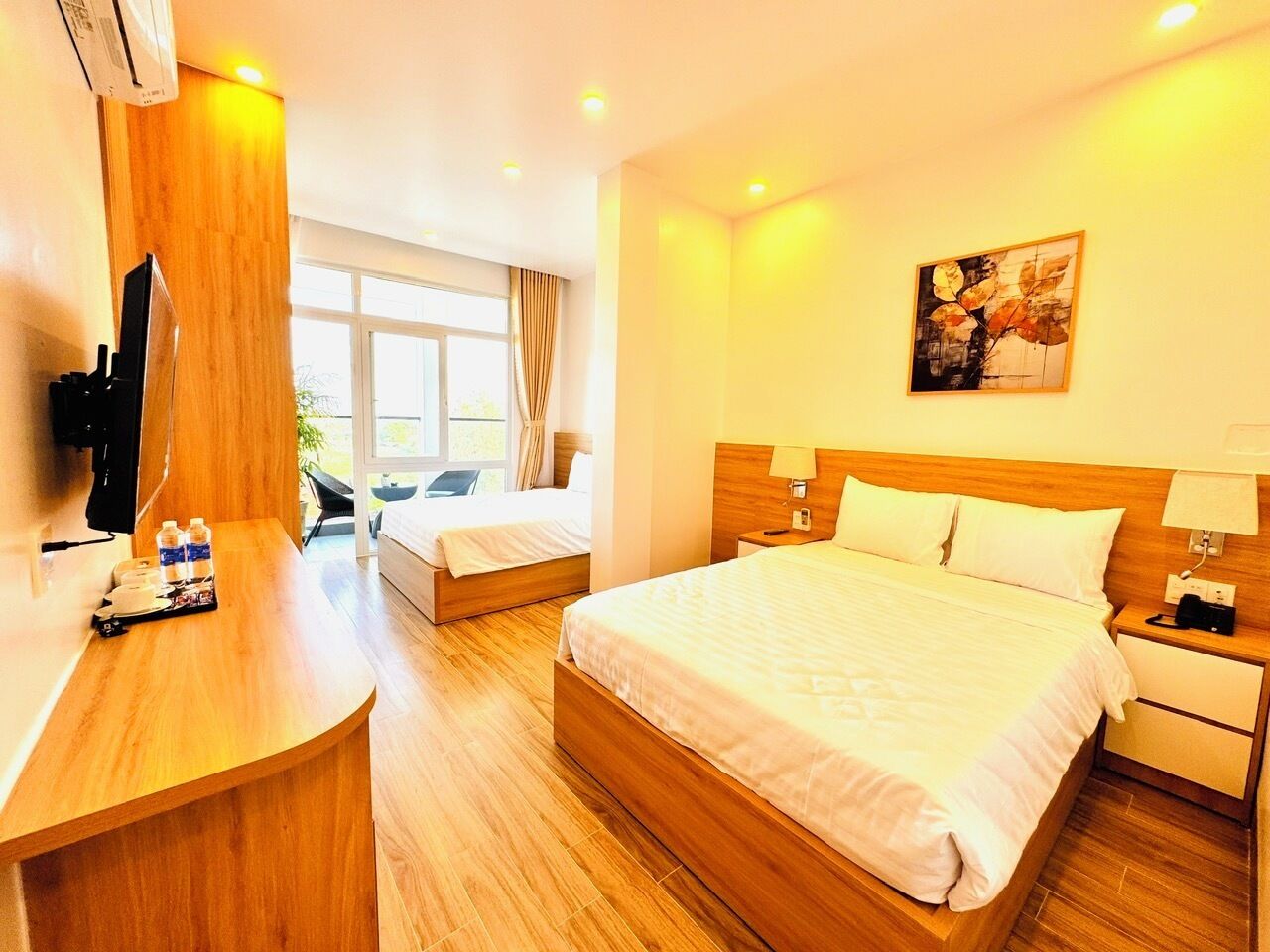 A hotel room with a large bed, a smaller bed, a desk with a chair, a TV, and a window with curtains.