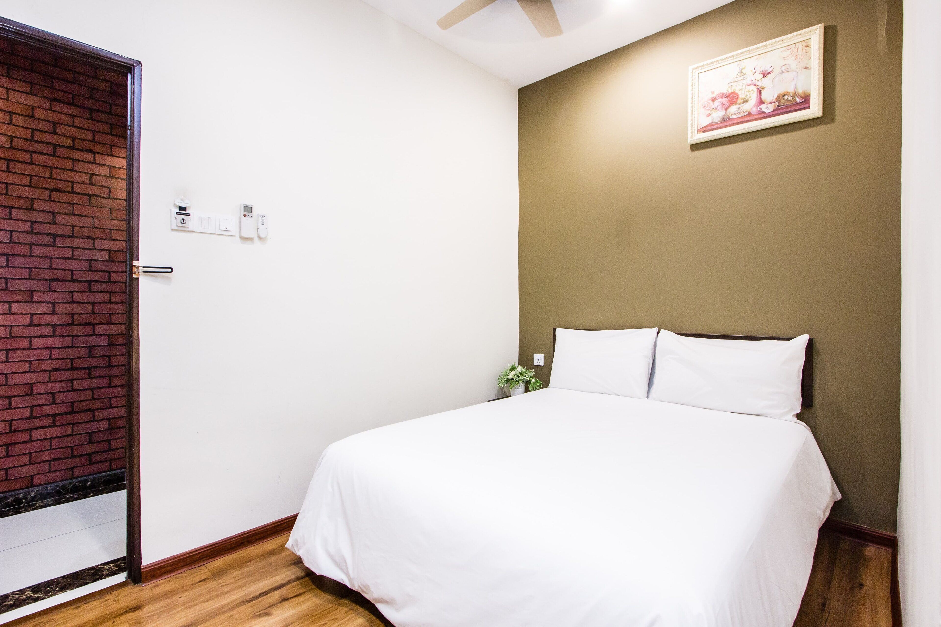 A bedroom with a bed, a door, a wall-mounted light switch, and a small plant.