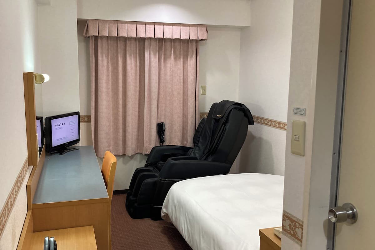 Ein Hotelzimmer mit einem Bett, einem Massagesessel, einem Schreibtisch mit Computer und einem fensterbepflanzten Fenster.