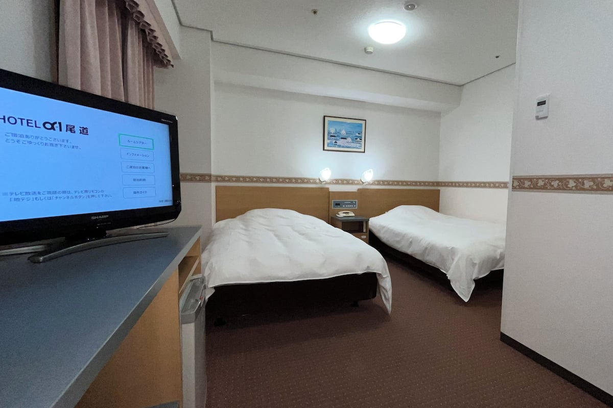 Ein Hotelzimmer mit zwei Betten, einem Schreibtisch mit Computer und einem an der Wand befestigten Fernseher, der einen Hotelordner anzeigt.