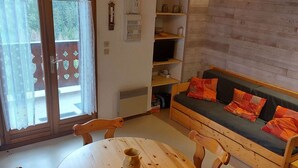 A cozy living area with a wooden sofa, a round wooden table, and a window with lace curtains.