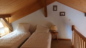 A small, cozy attic bedroom with two single beds, a wooden headboard, a small bedside table with a lamp, and a wooden railing.