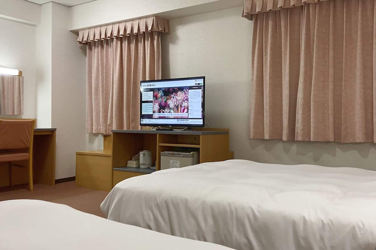 Ein Hotelzimmer mit Bett, Schreibtisch mit Computer und Vorhängen.