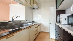 A modern kitchen with a stainless steel sink, wooden cabinets, a microwave, and a built-in oven. - Dai37 Matsui Building (Sapporo)