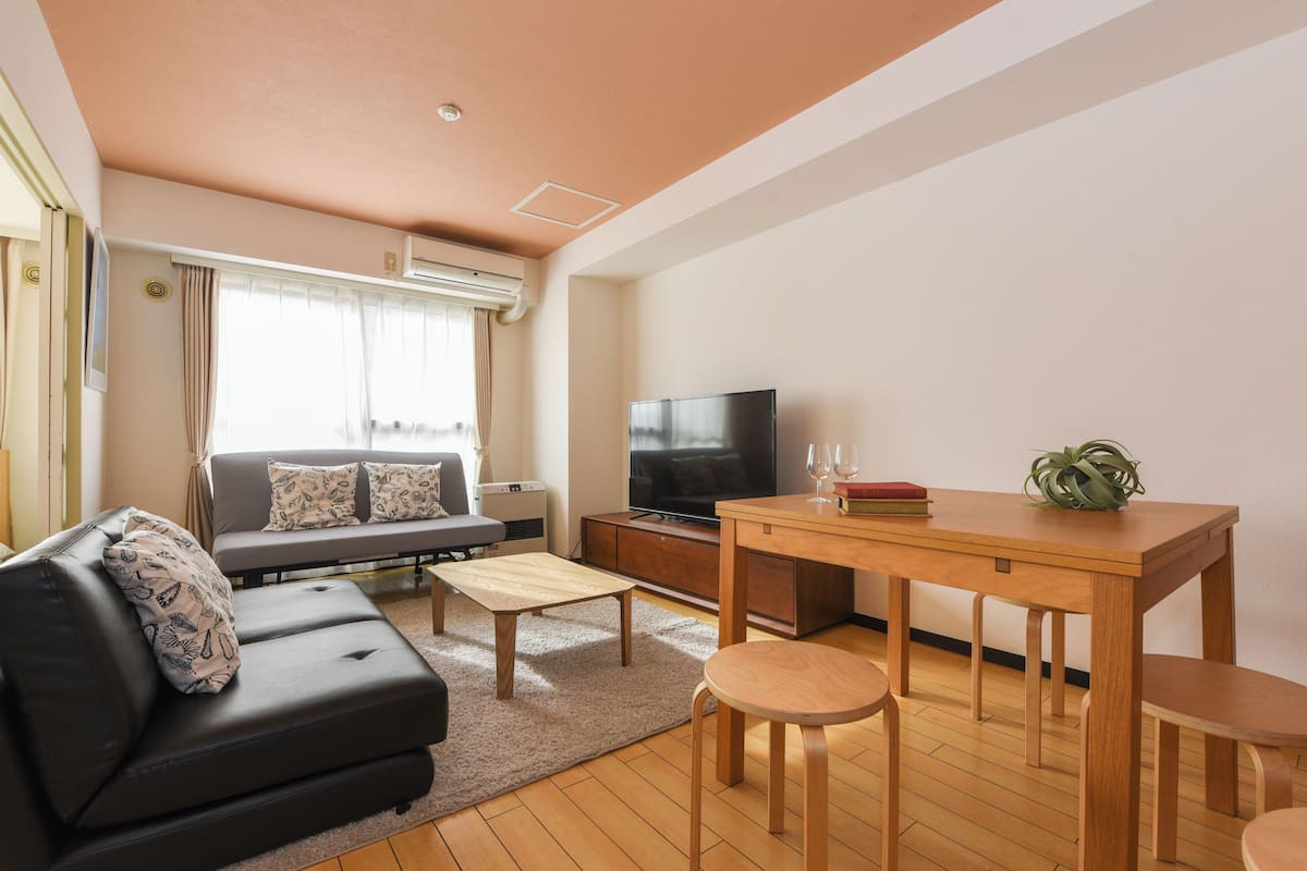 A modern living room with a sofa, a coffee table, a TV, and a dining table with chairs.