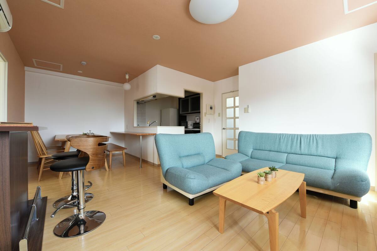 A modern living room with a blue sofa, a wooden coffee table, and a bar stool.