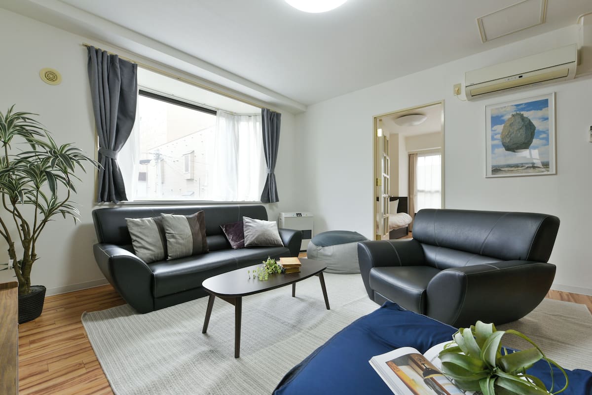 A modern living room with a sofa, armchair, coffee table, and a potted plant.