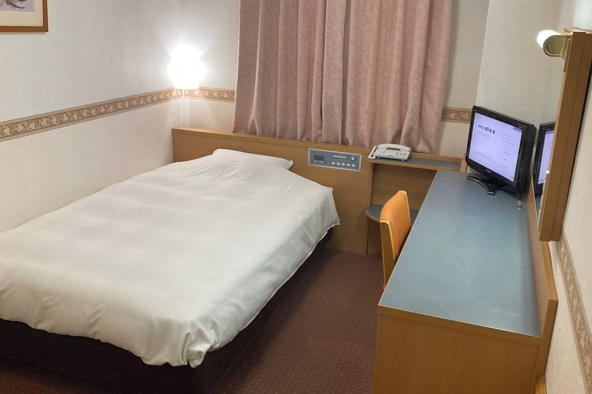 A hotel room with a single bed, a desk with a computer, and a telephone.