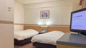 Habitación de hotel con dos camas, un escritorio, televisión, mesita de noche y termostato en la pared.