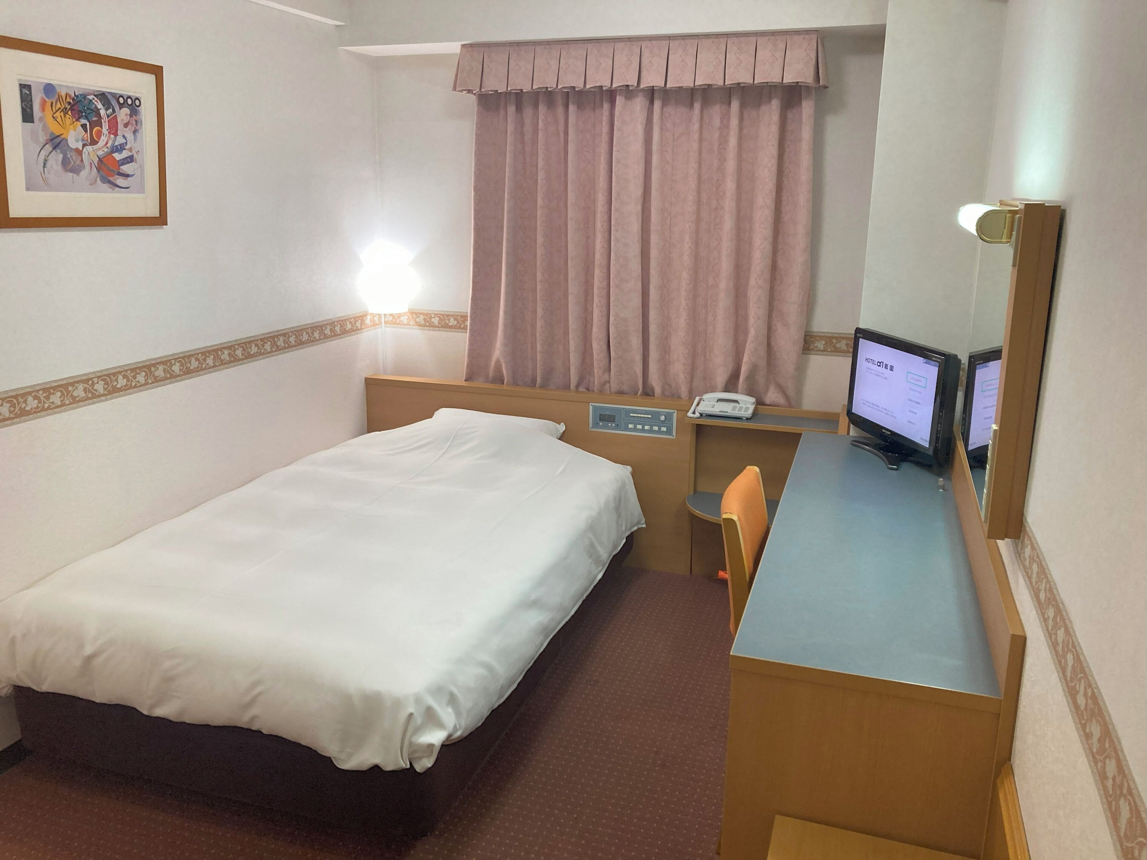 Habitación de hotel con cama, escritorio, silla y monitor de computadora.