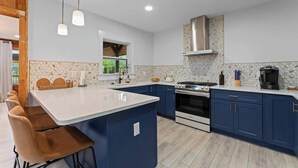 A modern kitchen with a large island, dark blue cabinets, and a stainless steel range hood. - The Cheswick A I Team Joseph Ellen (Orange Park)