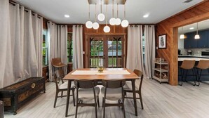A dining area with a wooden table, chairs, a chandelier, and a view of the outdoors. - The Cheswick A I Team Joseph Ellen (Orange Park)