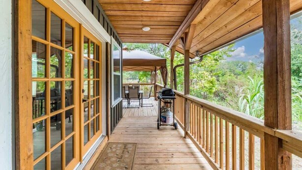 A covered porch with wooden railings, a grill, and a view of greenery. - The Cheswick A I Team Joseph Ellen (Orange Park)