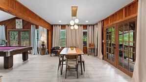 A spacious room with a pool table, a dining table with chairs, a lamp, and a view through large windows. - The Cheswick A I Team Joseph Ellen (Orange Park)