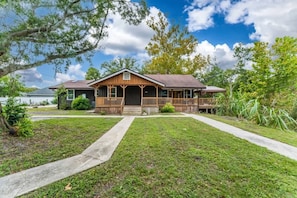 A two-story wooden house with a porch, a front yard, and a pathway leading to the entrance.