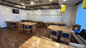 A room with wooden tables and chairs, a television on the wall, and a yellow hanging light fixture. - Hotel Alpha-One Izumo (Izumo)