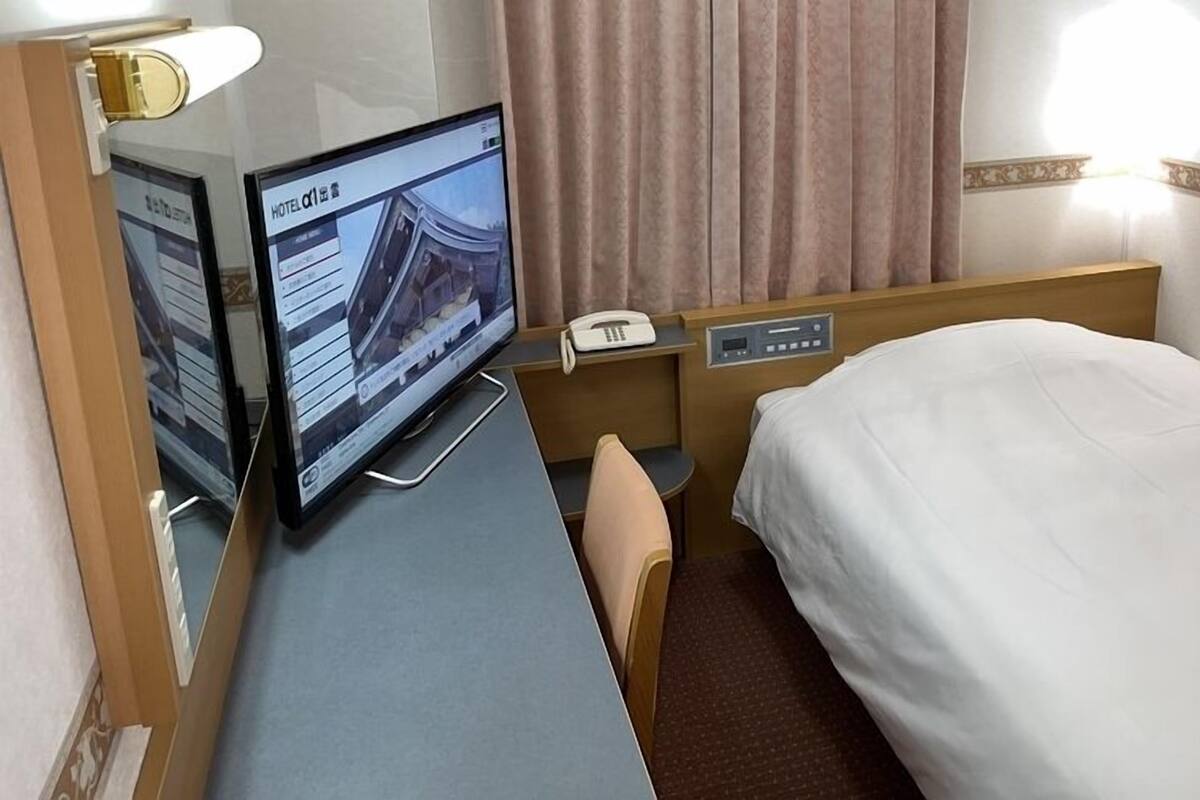 A hotel room with a bed, a desk with a computer, a telephone, and a window with curtains.