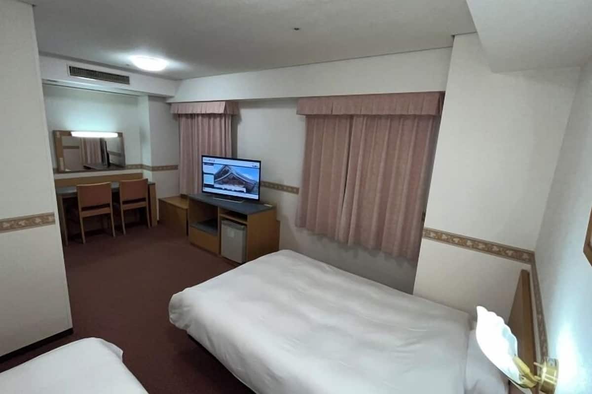 A hotel room with a bed, a desk with a computer, a chair, and a television.
